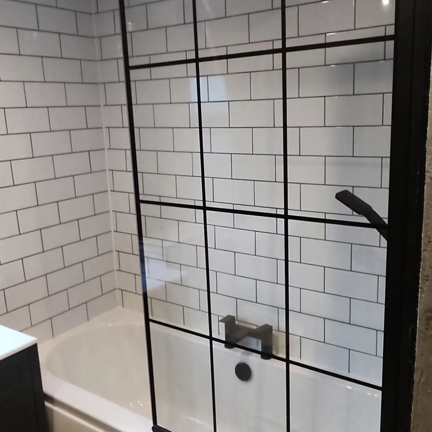 Bathroom with white metro tiles, a black-framed shower screen and black fittings over a bath