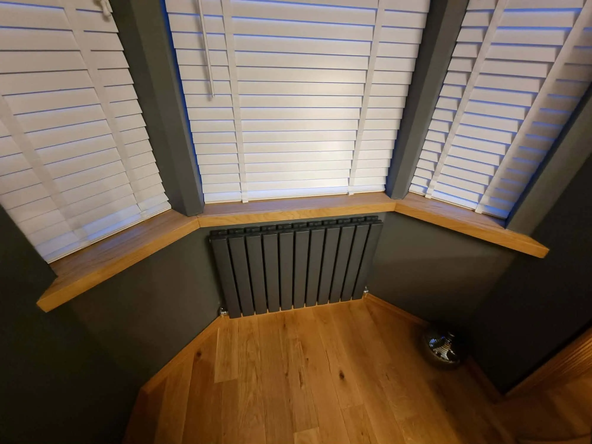 Bay window with white shutters, a timber window seat or sill, a radiator and a timber floor