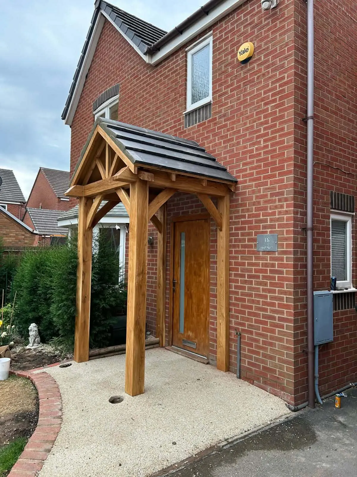 Timber entrance porch with a pitched tiled roof and bracing, in front of a red brick house