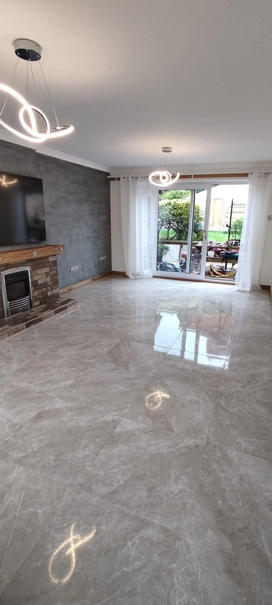 Room with large-format glossy floor tiles, a feature pendant light and garden doors