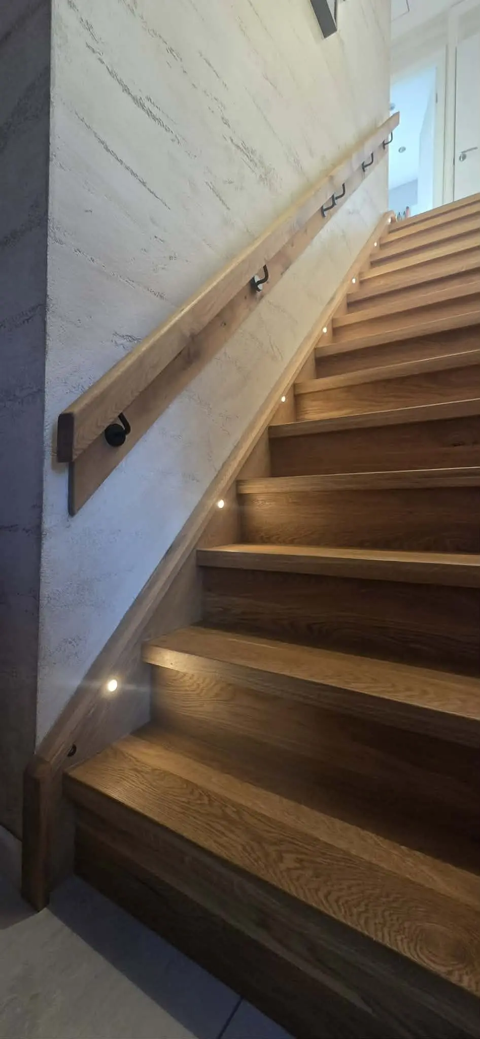 Timber staircase with a wall-mounted handrail and small lights set into the side of the stair
