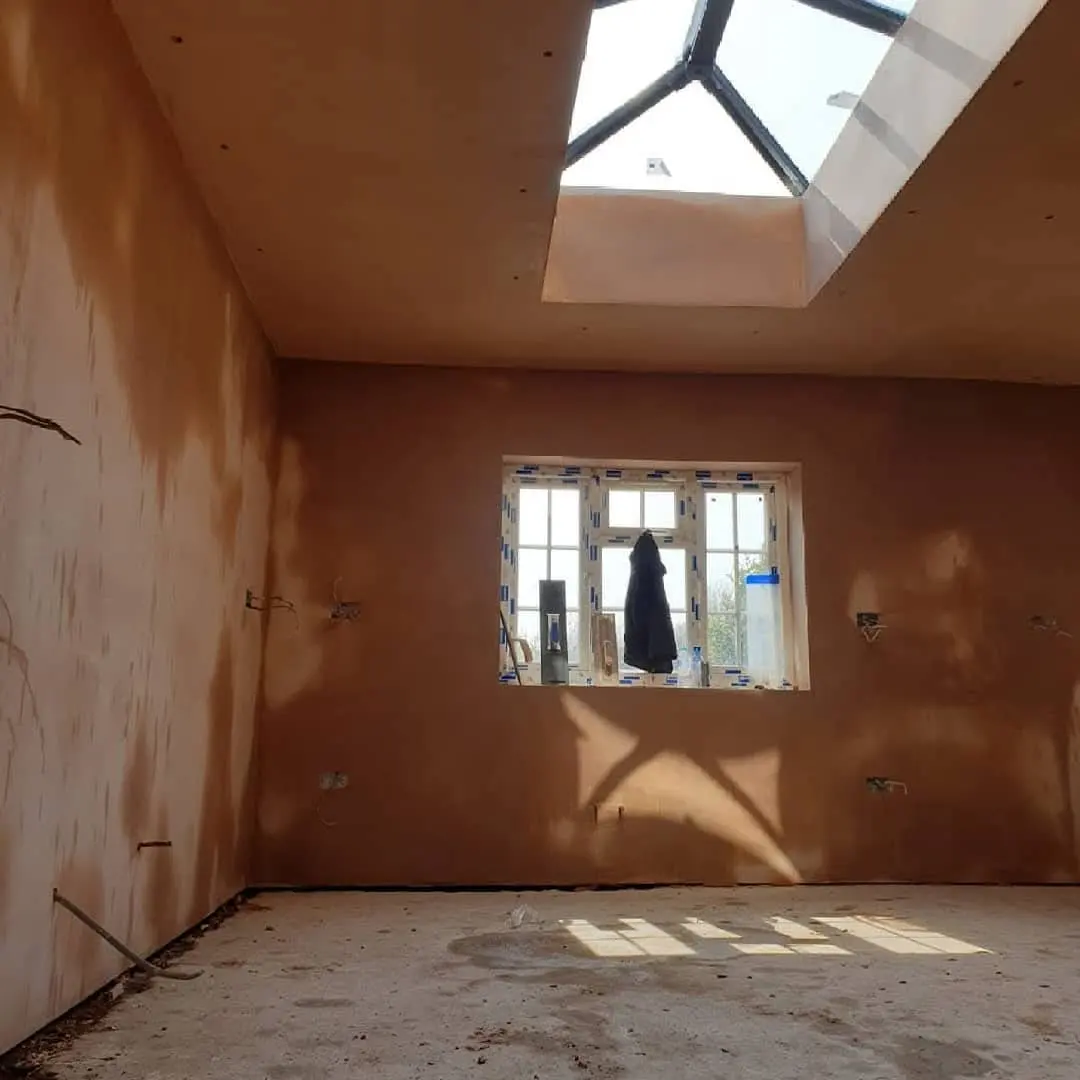 Room with fresh plaster on the walls, a roof light and a window, with the floor not yet finished