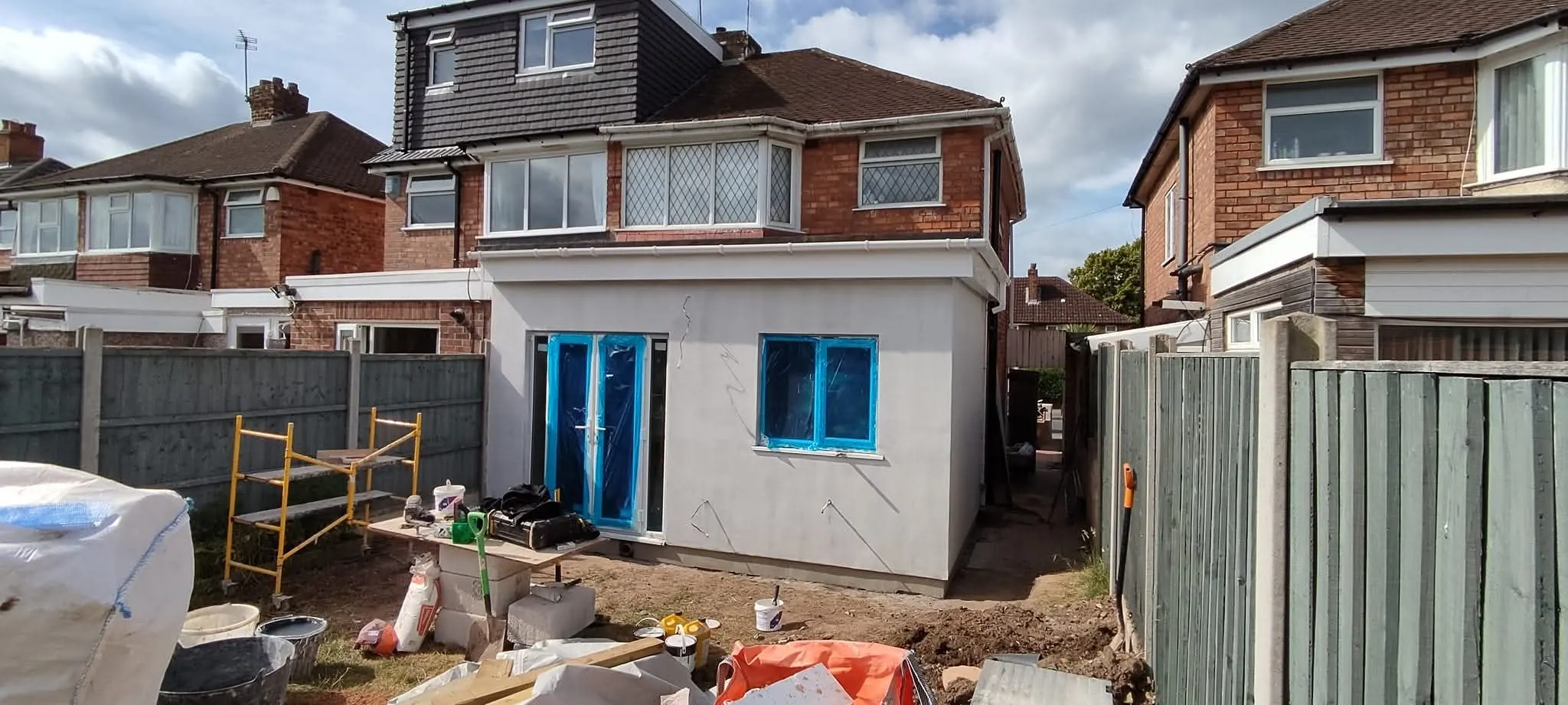 Rear of a house with a single-storey extension under construction, scaffolding and blue-framed openings